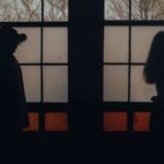 Two silhouettes standing back to back by a window, poem about love illusion and emotional distance