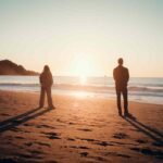 Two silhouettes standing apart on a beach at sunset, poem for him about one sided love and distance